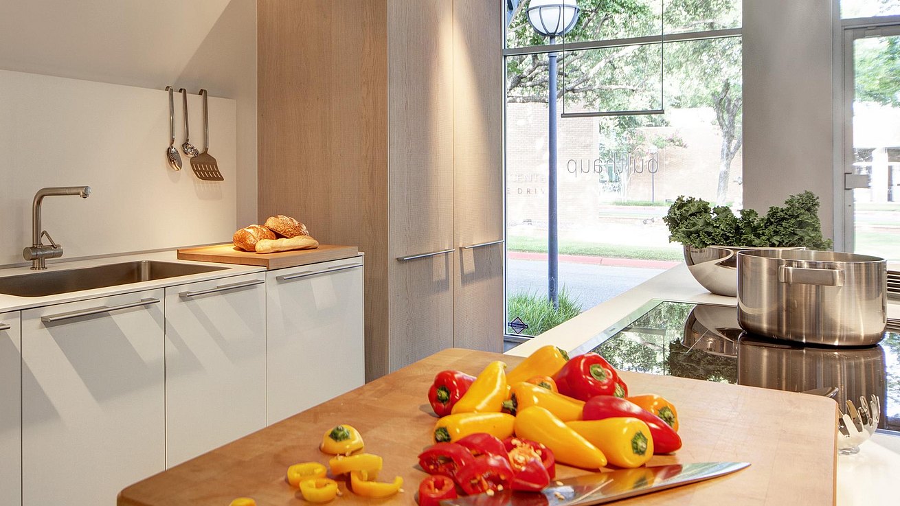 Detail of b3 kitchen in white laminate and oak featuring bulthaup chopping block with red and yellow peppers in the midst of being chopped.